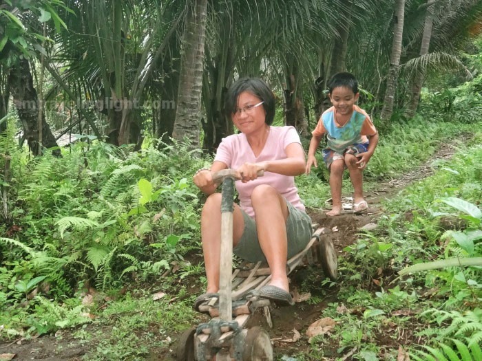 woman in ligiron riding downhill with kid cheering on, contraption like wooden bike, four wheels, Valencia, Negros Oriental